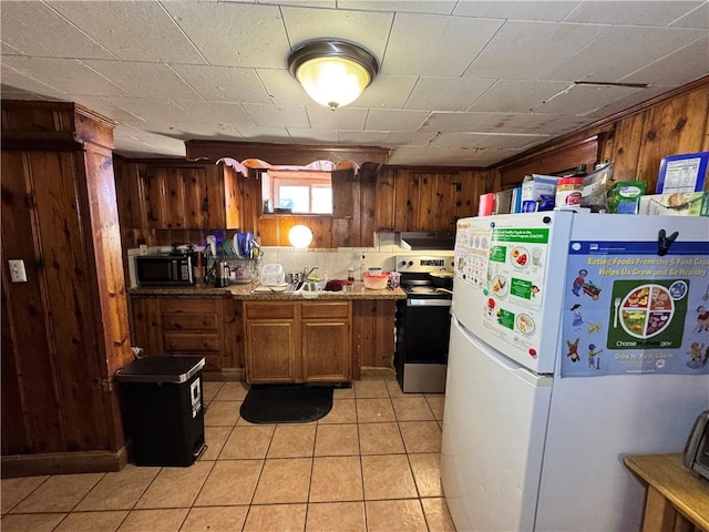 kitchen with black microwave, light tile patterned floors, wooden walls, stainless steel range with electric cooktop, and freestanding refrigerator