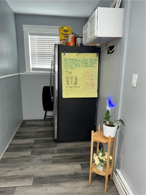 interior space featuring a baseboard heating unit, freestanding refrigerator, white cabinetry, and wood finished floors