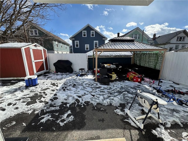 snowy yard featuring a storage shed, a gazebo, an outbuilding, and fence