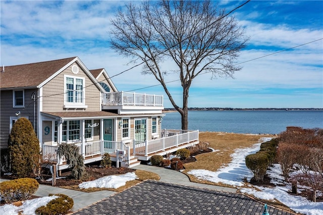 view of front facade with a porch, a water view, a shingled roof, and a balcony