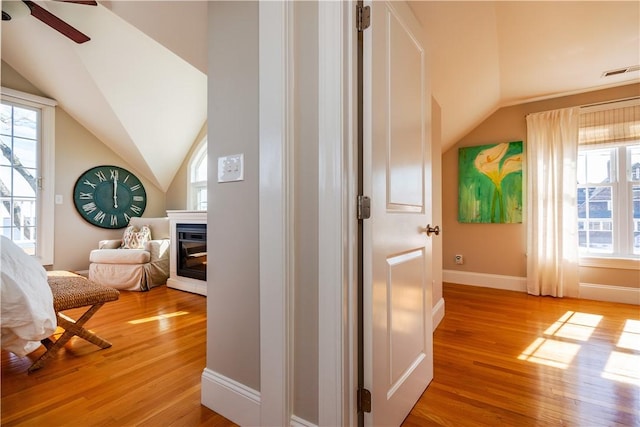 interior space with light wood-type flooring, visible vents, a glass covered fireplace, and lofted ceiling