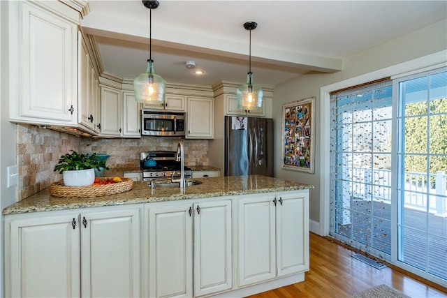 kitchen with stainless steel appliances, a peninsula, a sink, backsplash, and light wood finished floors