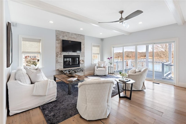 living room with visible vents, baseboards, light wood-type flooring, beam ceiling, and a tiled fireplace