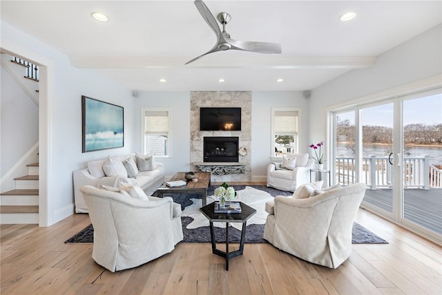 living area featuring light wood-style flooring, a fireplace, stairway, and beam ceiling