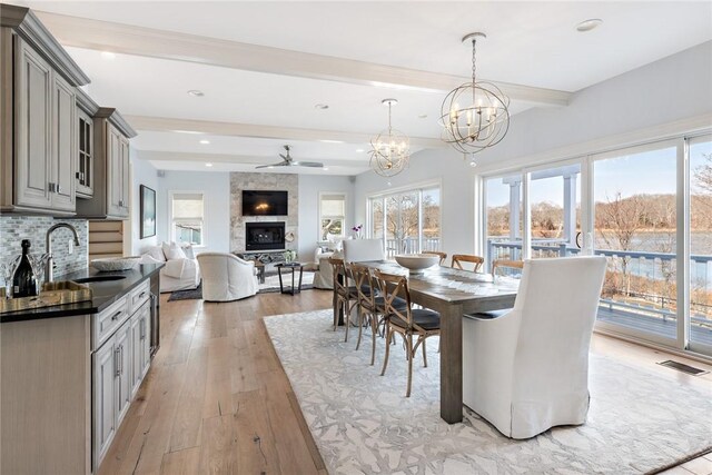 1040 Buttonwoods Ave, Warwick, RI 02886 - dining room with beamed ceiling, a large fireplace, light wood-type flooring, ceiling fan, and a chandelier