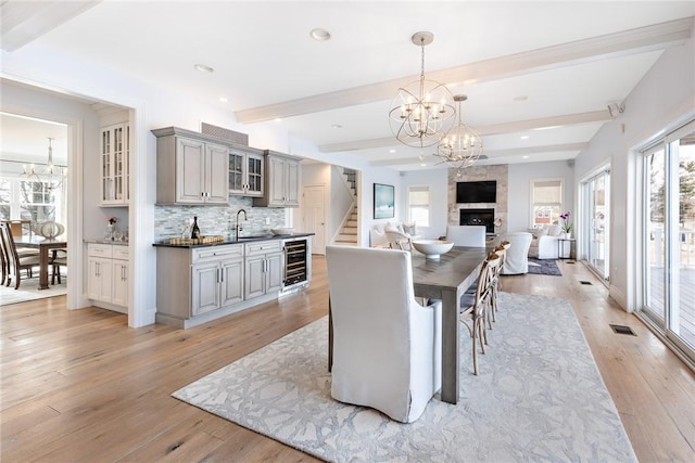 dining space featuring a healthy amount of sunlight, an inviting chandelier, wine cooler, and beamed ceiling