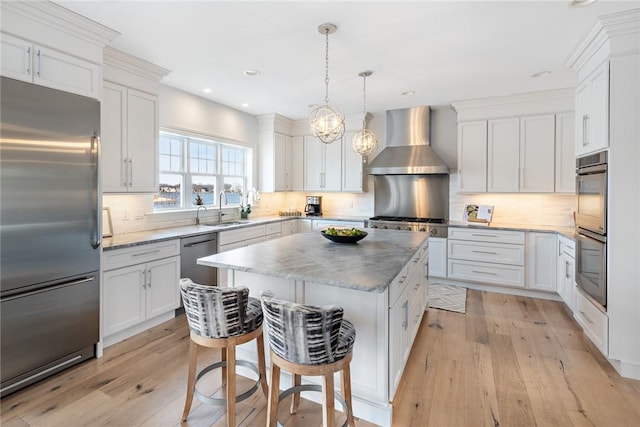 kitchen featuring a sink, white cabinets, appliances with stainless steel finishes, wall chimney range hood, and a center island