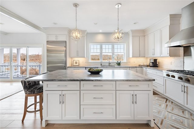 kitchen featuring stainless steel appliances, a sink, a kitchen island, white cabinetry, and wall chimney exhaust hood