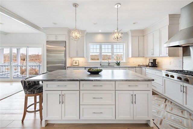 1040 Buttonwoods Ave, Warwick, RI 02886 - kitchen with appliances with stainless steel finishes, wall chimney range hood, a kitchen island, a chandelier, and white cabinetry