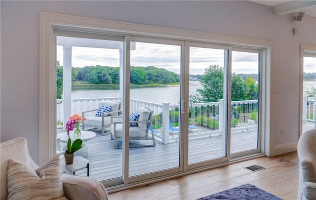 doorway featuring a water view, visible vents, baseboards, beam ceiling, and light wood finished floors