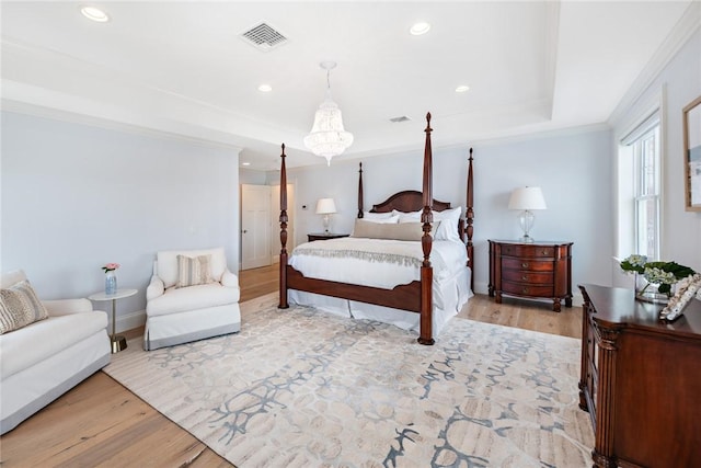 bedroom featuring light wood-style floors, visible vents, a tray ceiling, and ornamental molding