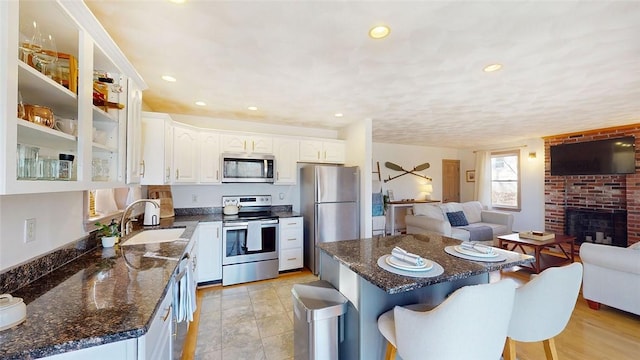 kitchen featuring glass insert cabinets, open floor plan, appliances with stainless steel finishes, white cabinets, and a sink