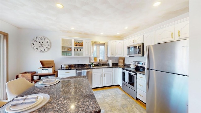 kitchen featuring appliances with stainless steel finishes, white cabinetry, dark stone counters, and a sink