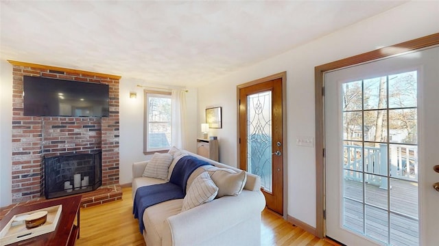 living room featuring a brick fireplace, baseboards, and light wood-type flooring