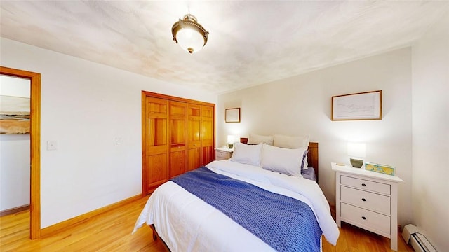 bedroom featuring a closet, light wood-style flooring, baseboards, and a baseboard radiator