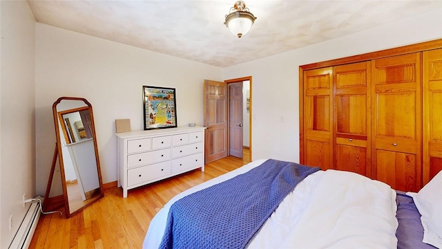 bedroom featuring a baseboard heating unit, light wood-style flooring, baseboards, and a closet