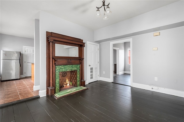 unfurnished living room with hardwood / wood-style floors, an inviting chandelier, a tile fireplace, and baseboards