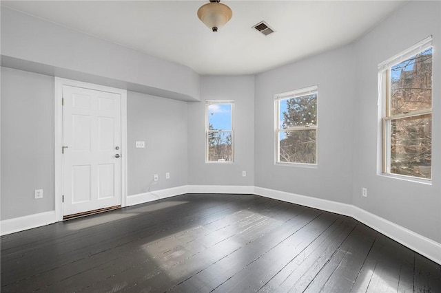 unfurnished room featuring dark wood-type flooring, visible vents, and baseboards