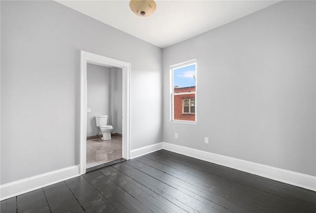 unfurnished bedroom with dark wood-type flooring, connected bathroom, and baseboards