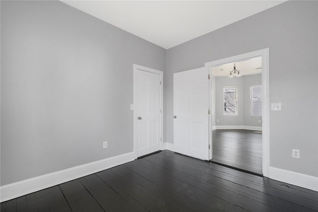 empty room featuring a chandelier, dark wood finished floors, and baseboards