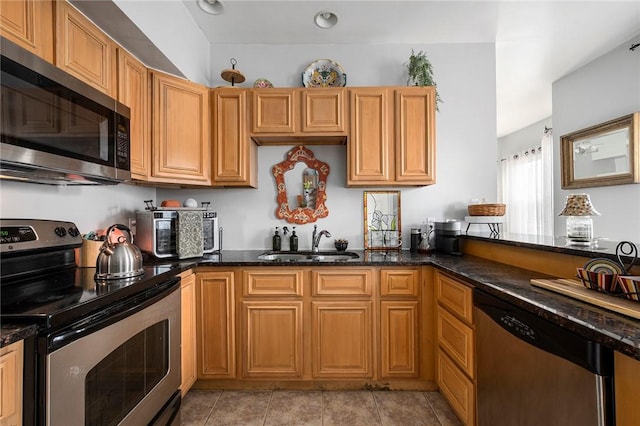 kitchen featuring appliances with stainless steel finishes, dark stone counters, a sink, and light tile patterned floors