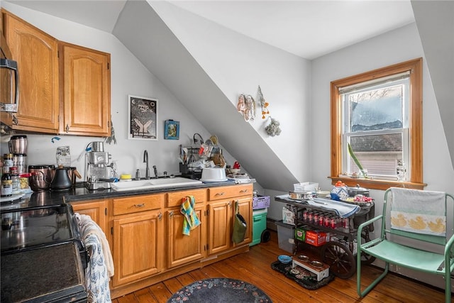 kitchen featuring a sink, vaulted ceiling, brown cabinets, black electric range oven, and wood-type flooring