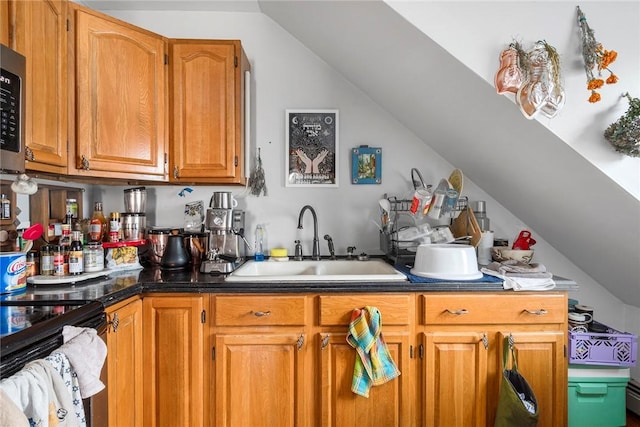 kitchen featuring brown cabinets, dark countertops, lofted ceiling, stainless steel microwave, and a sink