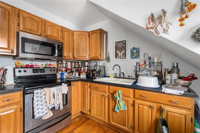 kitchen featuring brown cabinets, wood finished floors, vaulted ceiling, stainless steel appliances, and a sink