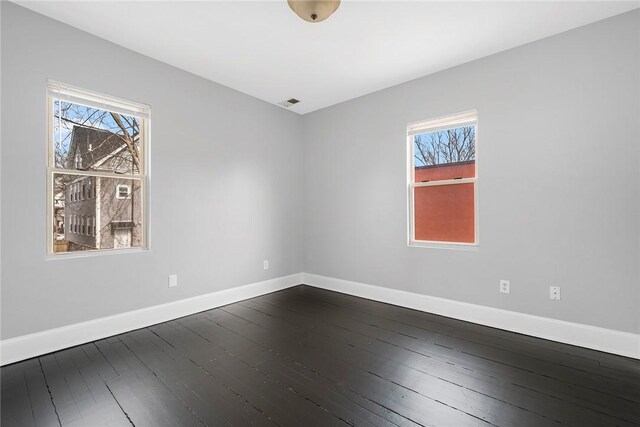 spare room featuring dark wood-style flooring, a healthy amount of sunlight, visible vents, and baseboards