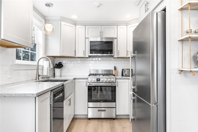 kitchen featuring decorative backsplash, light stone counters, appliances with stainless steel finishes, light wood-style floors, and a sink