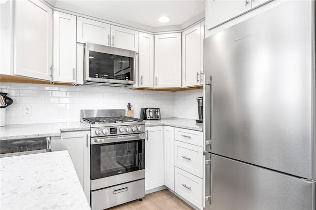 kitchen featuring white cabinets, tasteful backsplash, light stone counters, and stainless steel appliances