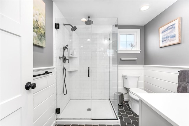 bathroom featuring tile patterned flooring, toilet, vanity, wainscoting, and a shower stall