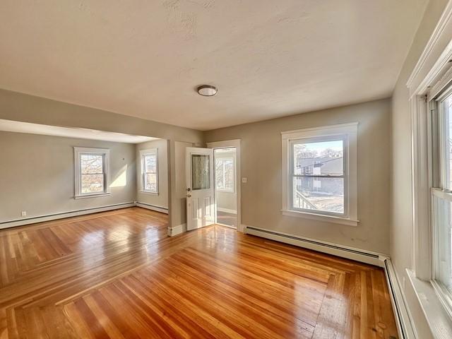 empty room featuring baseboard heating, wood finished floors, and baseboards