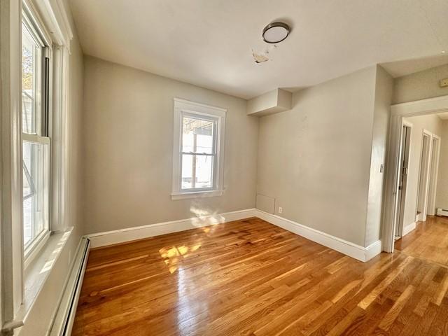 empty room with a baseboard heating unit, wood finished floors, and baseboards