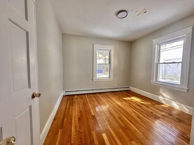 unfurnished room featuring a baseboard heating unit, baseboards, and hardwood / wood-style floors