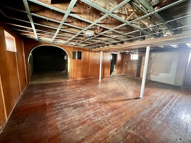 basement with arched walkways and hardwood / wood-style flooring