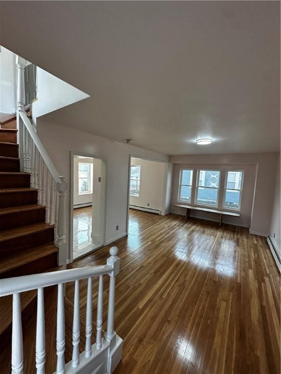 unfurnished living room with a baseboard radiator, stairway, baseboard heating, wood finished floors, and baseboards