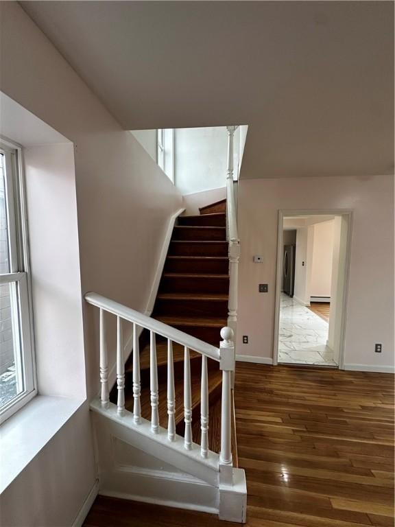 stairs featuring a healthy amount of sunlight, baseboards, baseboard heating, and wood finished floors