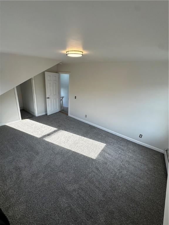 empty room with vaulted ceiling, baseboards, and dark colored carpet