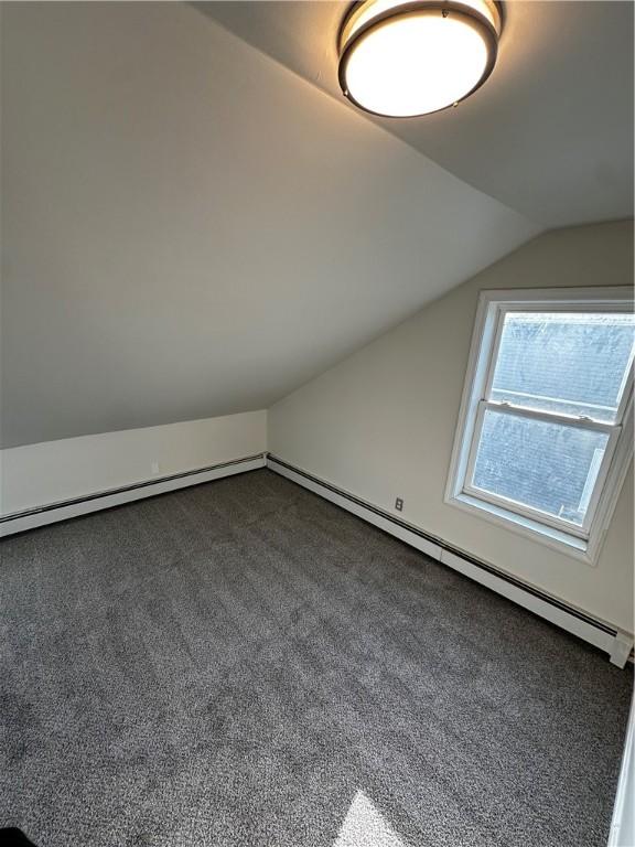 additional living space featuring vaulted ceiling, a baseboard heating unit, and dark colored carpet