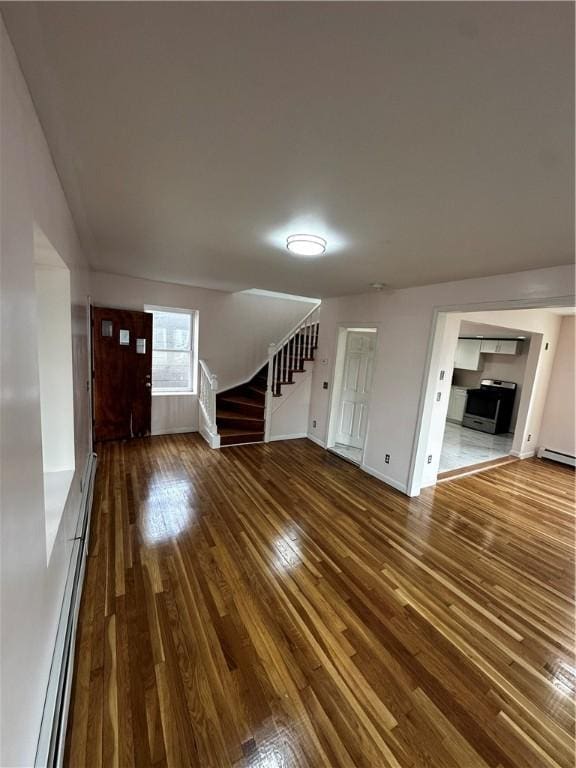 unfurnished living room featuring stairs, baseboard heating, wood finished floors, and baseboards