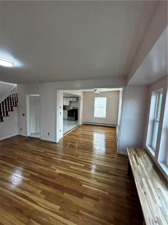 unfurnished living room featuring a baseboard radiator, baseboards, stairway, and wood finished floors