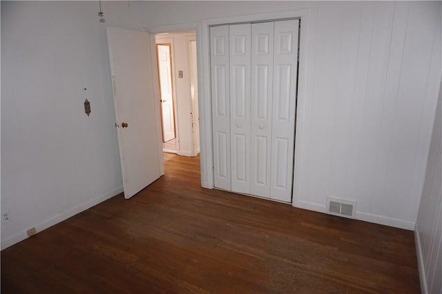 unfurnished bedroom featuring dark wood-type flooring, a closet, visible vents, and baseboards