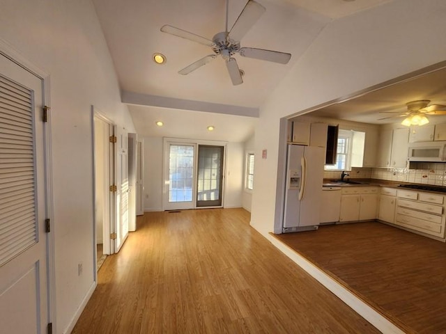 kitchen with lofted ceiling, dark countertops, a sink, wood finished floors, and white appliances