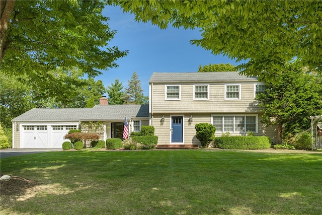 colonial inspired home with aphalt driveway, a garage, a chimney, and a front yard