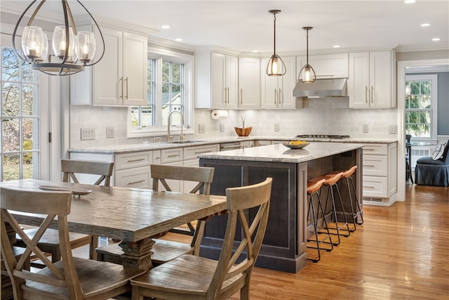 kitchen featuring a sink, light wood-style floors, under cabinet range hood, white cabinetry, and a center island