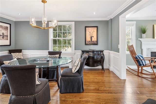 dining area with a tiled fireplace, crown molding, wood finished floors, and wainscoting