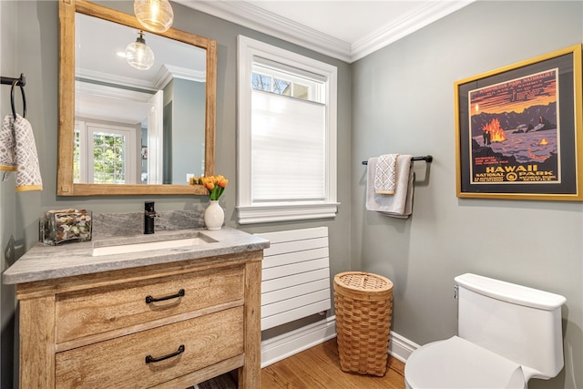 half bathroom with vanity, wood finished floors, baseboards, crown molding, and toilet