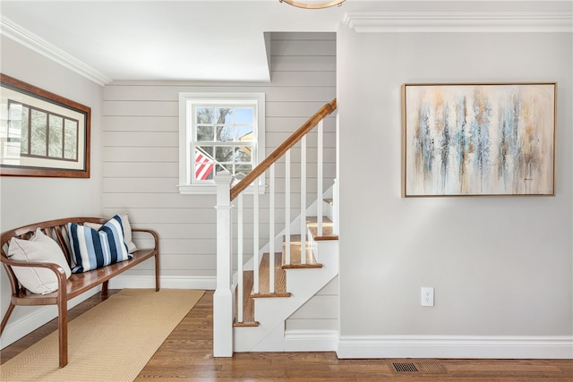 staircase featuring visible vents, ornamental molding, wood finished floors, wooden walls, and baseboards