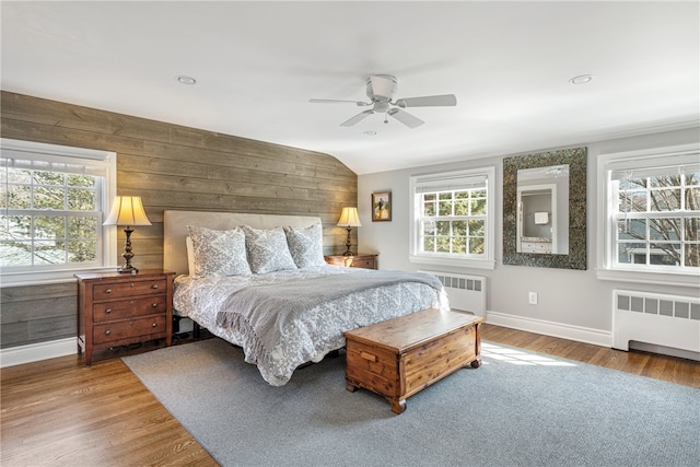 bedroom featuring baseboards, wood finished floors, radiator heating unit, and wood walls